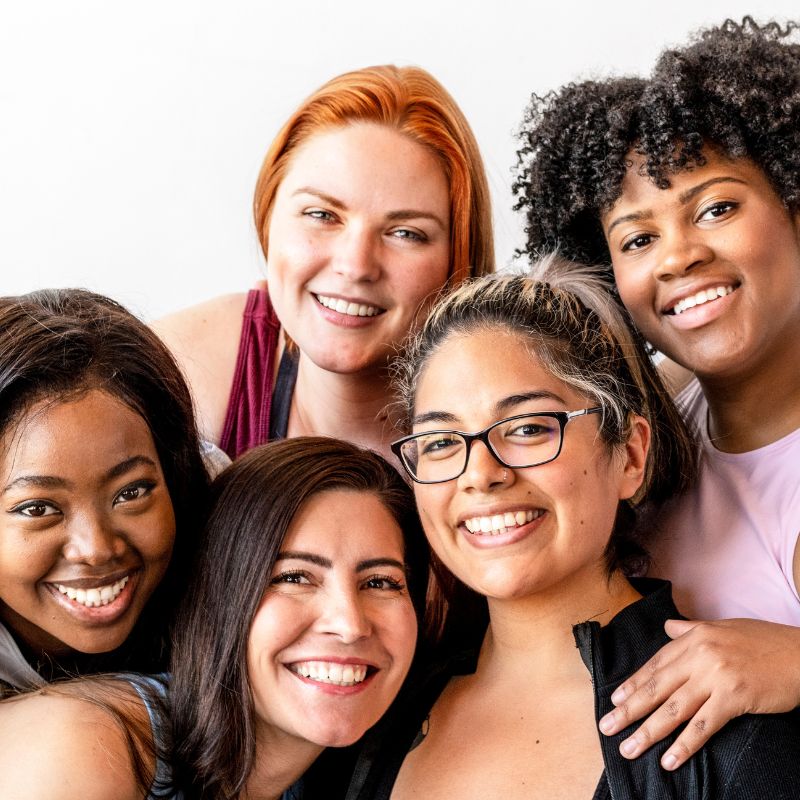 Group of diverse women smiling together, representing community, connection, and empowerment.

