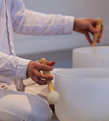 Person playing crystal singing bowls during a sound healing session, using mallets to create soothing, vibrational energy for relaxation and holistic wellness.