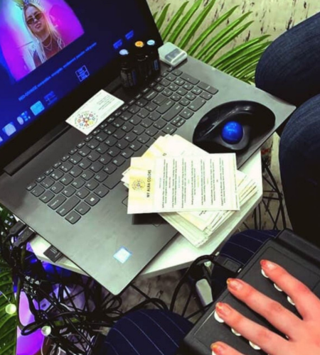Hand placed on a biometric scanner during an aura and energy reading session at My Healing Suite, with a laptop displaying colorful aura imaging, essential oils, wellness cards, and greenery in the background.