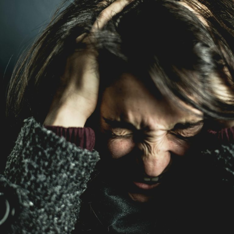 Close-up of a woman in distress with eyes closed and hands in hair, expressing anxiety.
